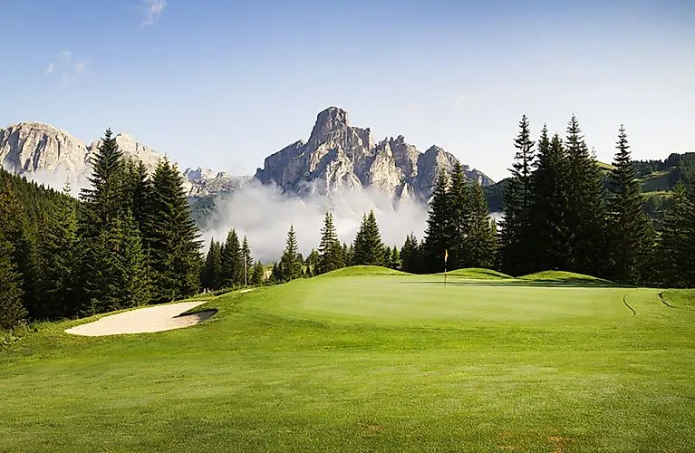 Weelderig groene golfbaan tegen een dramatische bergachtergrond in de Dolomieten bij Corvara.