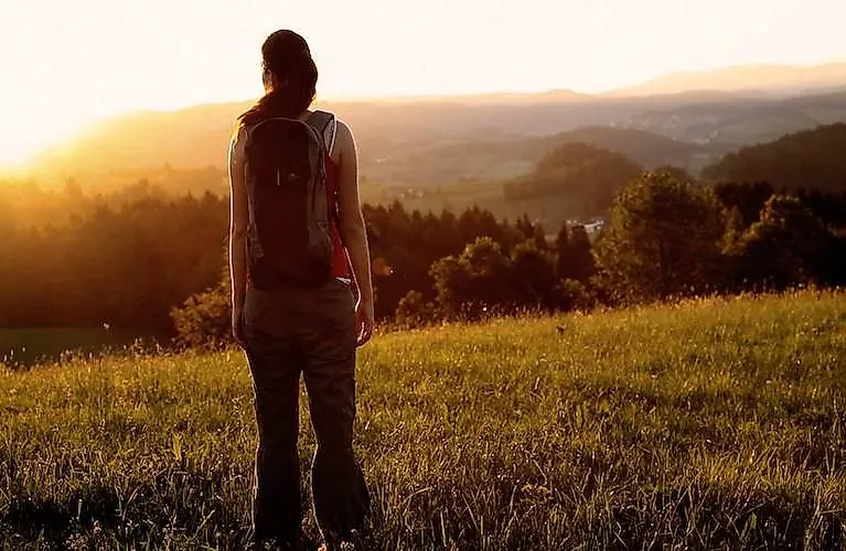 Frau mit Rucksack blickt bei Sonnenuntergang über das Ilztal und die Hügel
