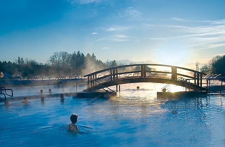 Menschen genießen das warme Wasser der Chiemgau Thermen in Bad Endorf bei Sonnenuntergang mit Blick auf die Berge