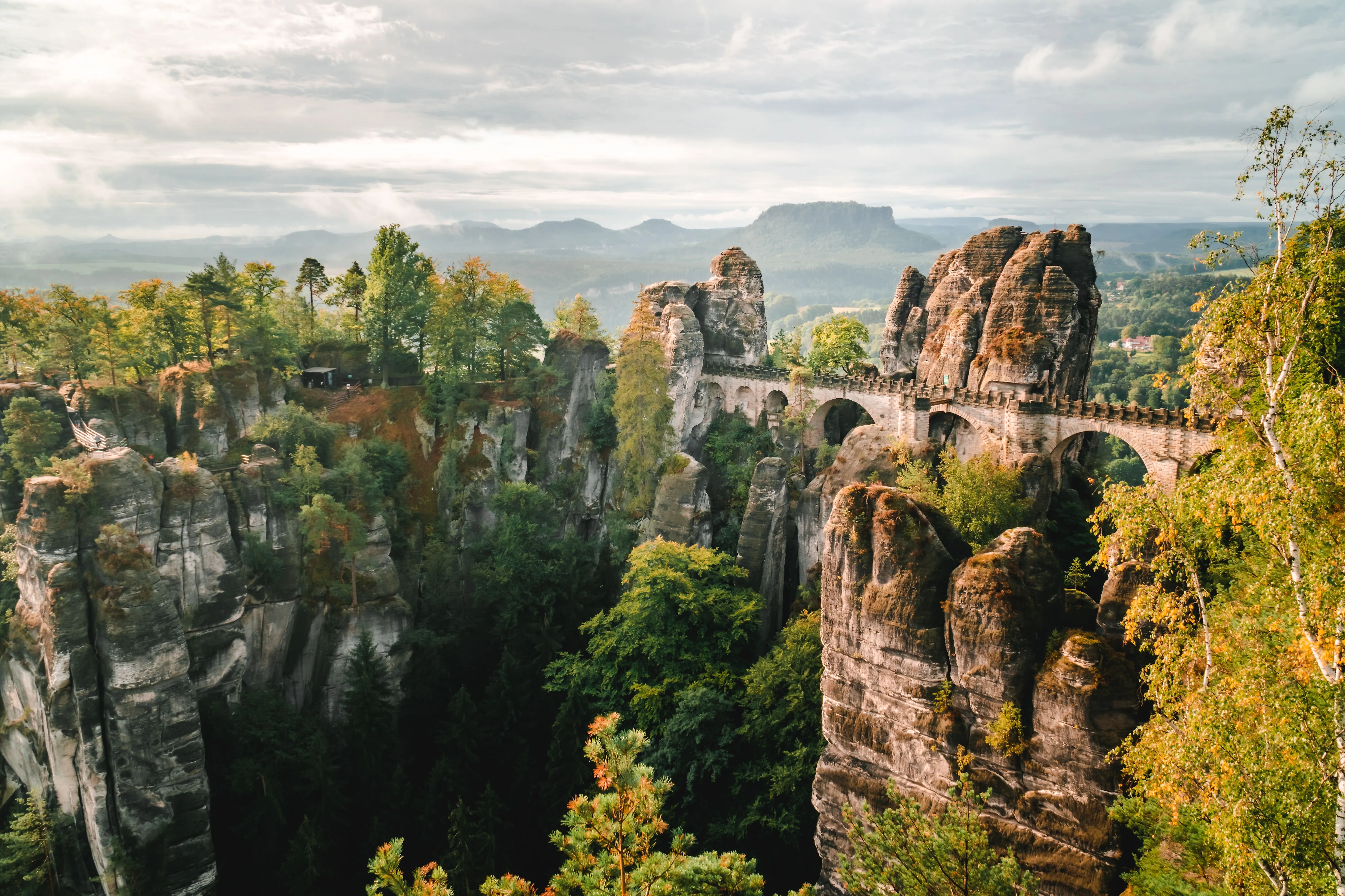 Panoramaaufnahme der Basteibrücke im Elbsandsteingebirge in der Nähe von Bad Schandau, umgeben von markanten Felsformationen und herbstlich gefärbtem Wald.