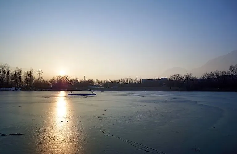 Winterliche Stimmung am gefrorenen Baggersee in Innsbruck bei Sonnenuntergang mit Blick auf die verschneiten Berge.
