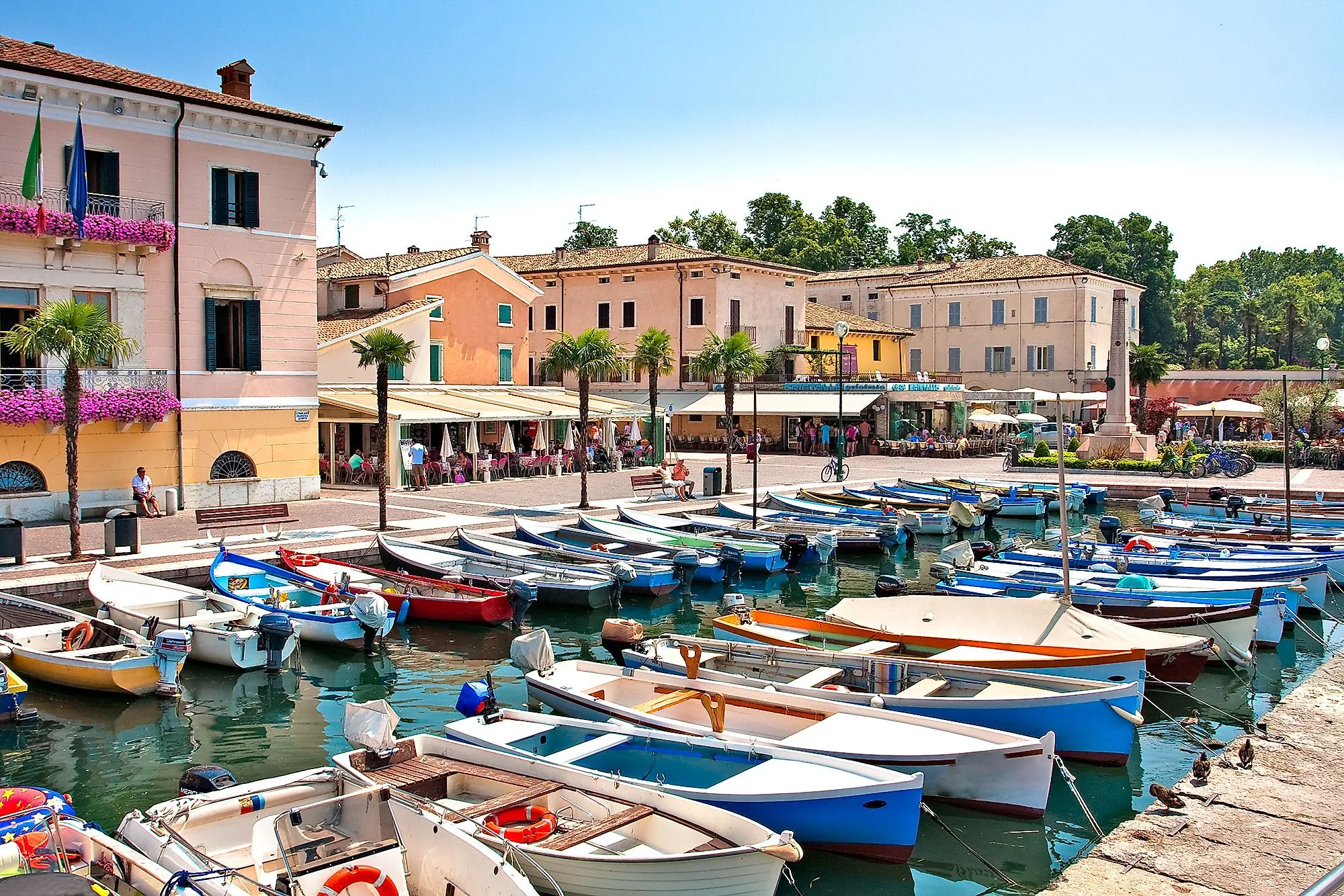 Boote im Hafen von Bardolino am Gardasee, umgeben von historischen Gebäuden und Palmen.