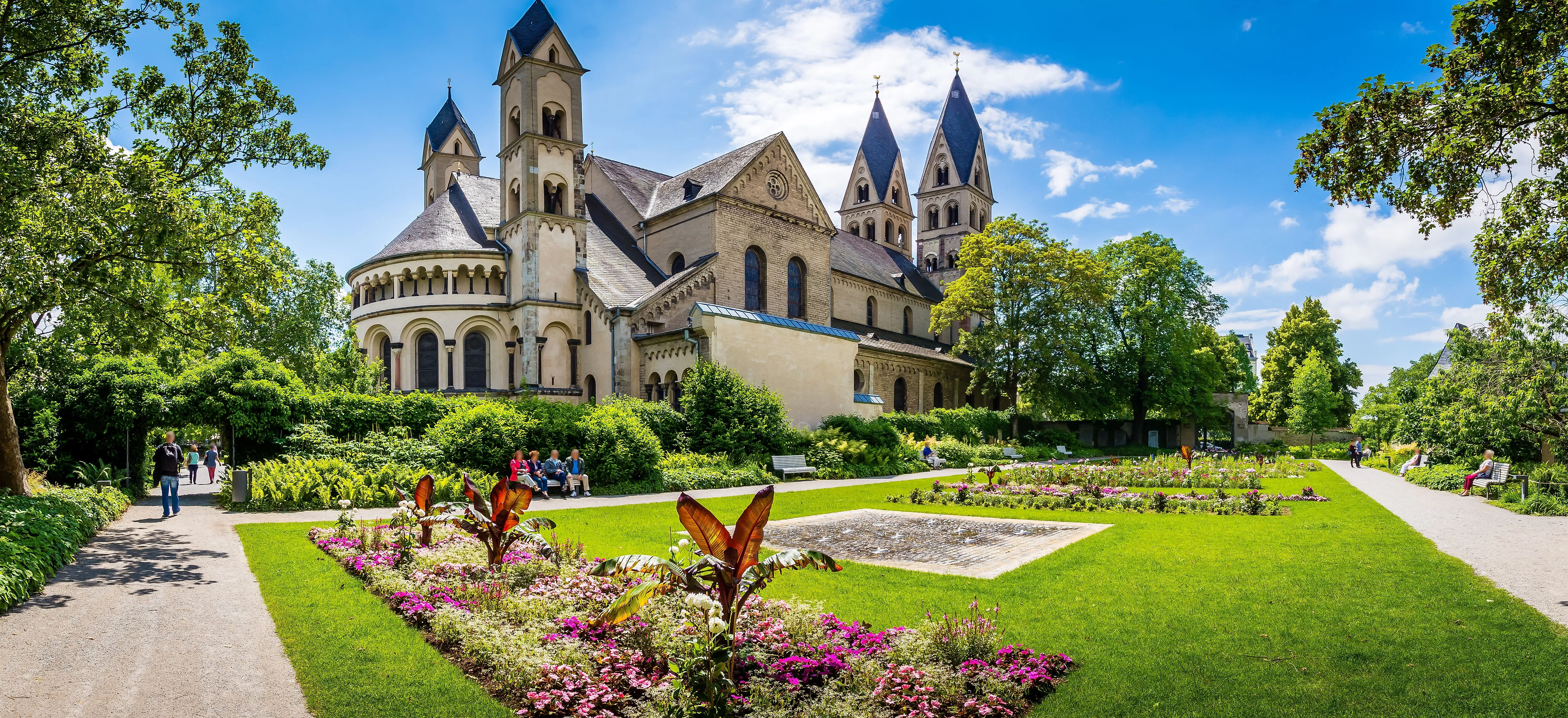 Romanische Basilika St. Kastor in Koblenz mit gepflegter Gartenanlage an einem sonnigen Tag.