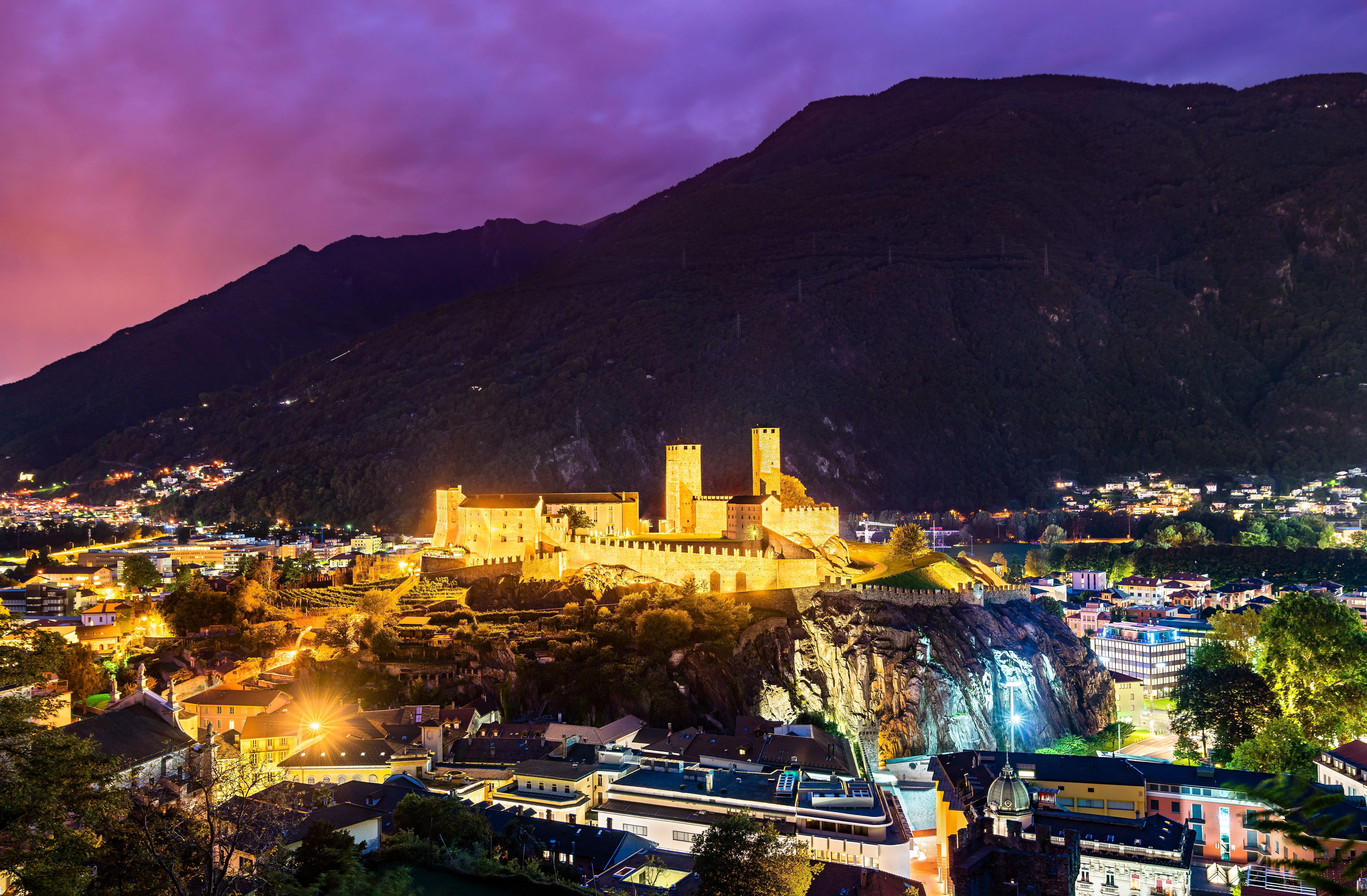Castelgrande in Bellinzona bei Nacht, festlich beleuchtet vor dunklen Berghängen und Abendhimmel