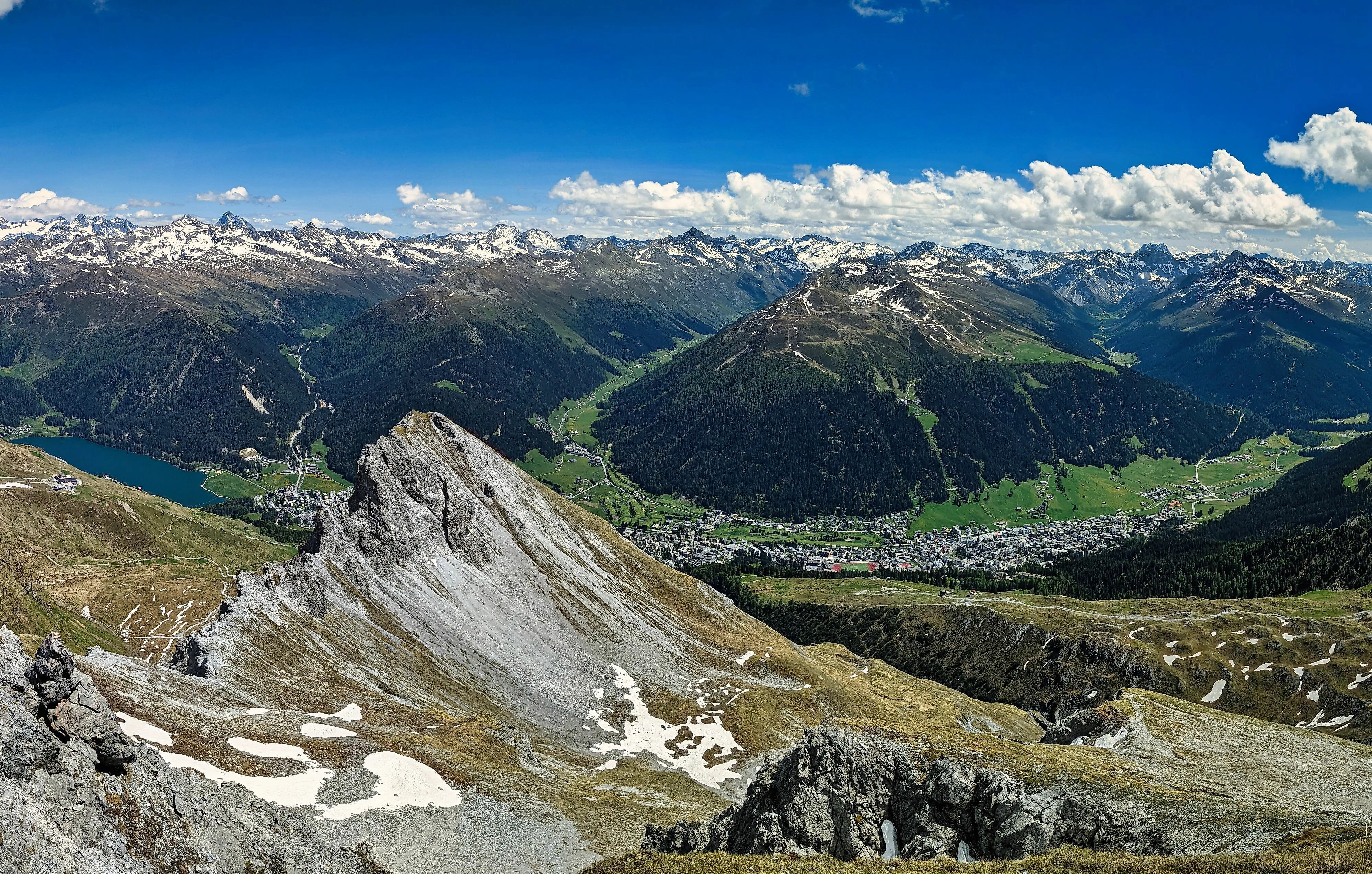 Panoramablick auf Davos-Dorf und umliegende Alpenlandschaft mit See, Tälern und schneebedeckten Berggipfeln.