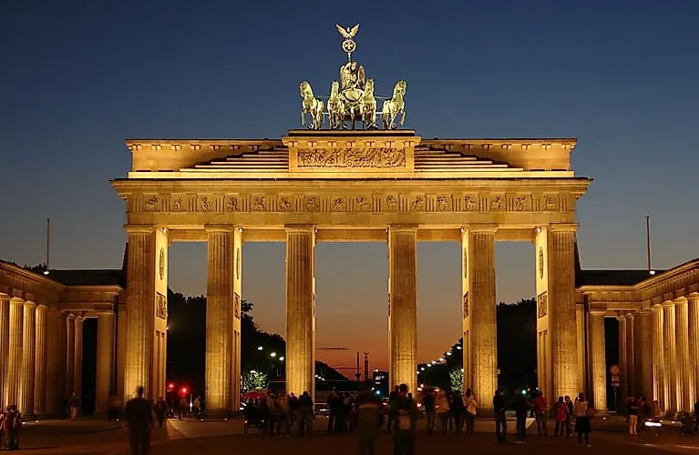 Brandenburger Tor in Berlin bei Abenddämmerung mit beleuchteter Quadriga und Besuchern im Vordergrund.