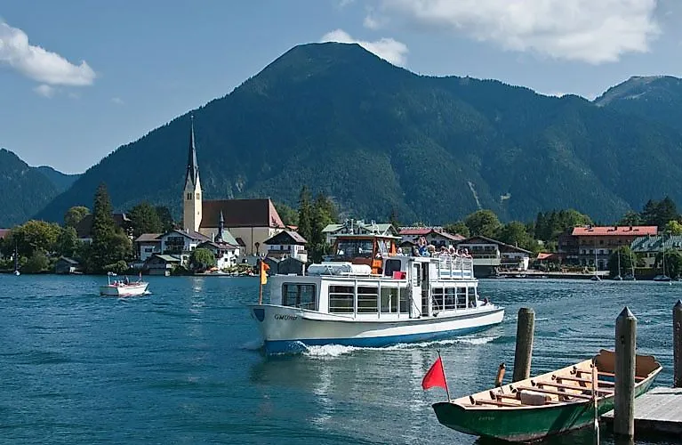 Ausflugsschiff auf dem Tegernsee mit Blick auf den Ort und die umliegenden Berge an einem sonnigen Sommertag.