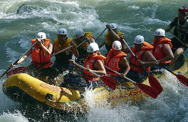 Gruppe beim Wildwasser-Rafting auf einem reißenden Fluss in Flachau im Sommer, ausgerüstet mit Helmen und Schwimmwesten.