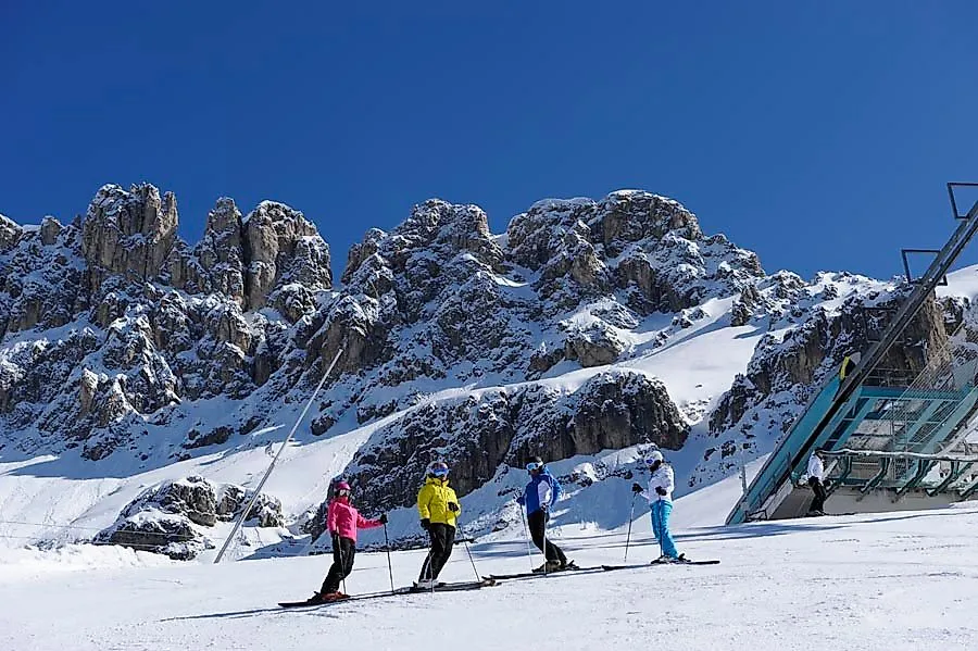 Skigroep op een zonnige piste in het Carezza skigebied tegen een indrukwekkende rotsachtige achtergrond