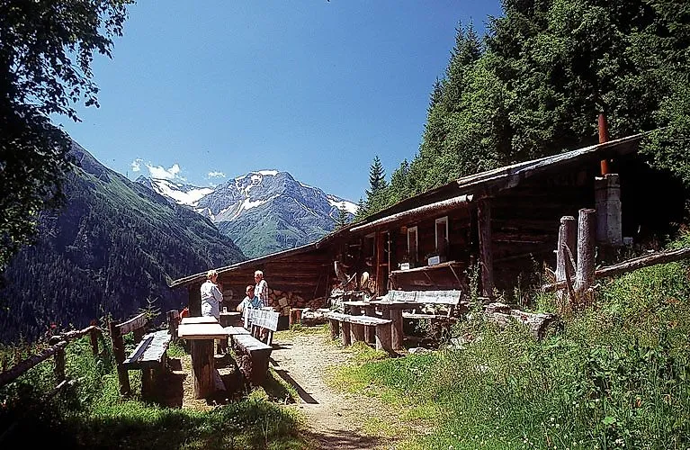 Wanderer rasten an einer urigen Alm im Gasteiner Tal mit Blick auf die grünen Berghänge und verschneite Gipfel im Hintergrund.