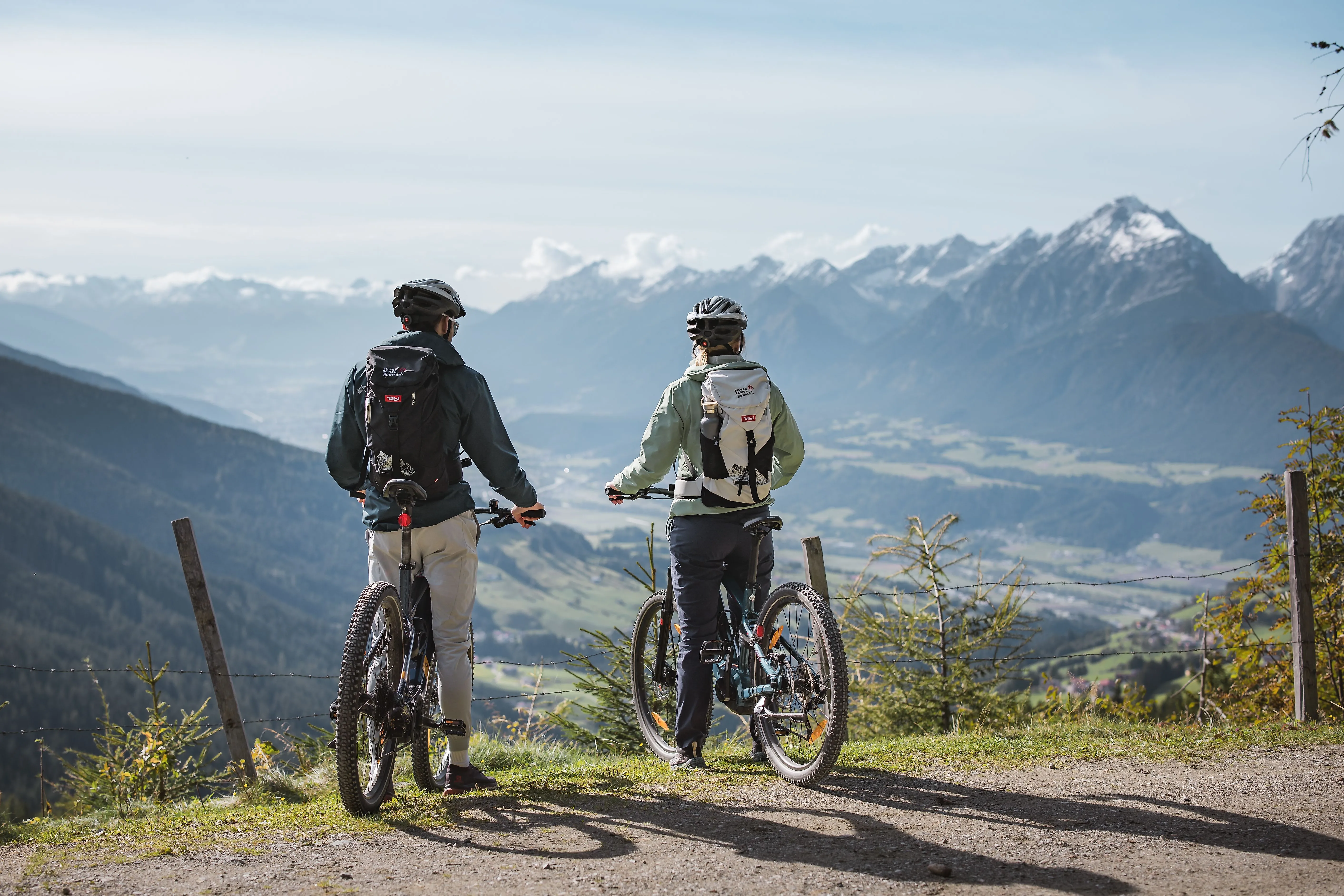 Zwei Mountainbiker mit Fahrrädern auf Aussichtspunkt mit Blick auf Tal und Alpenpanorama im Hintergrund