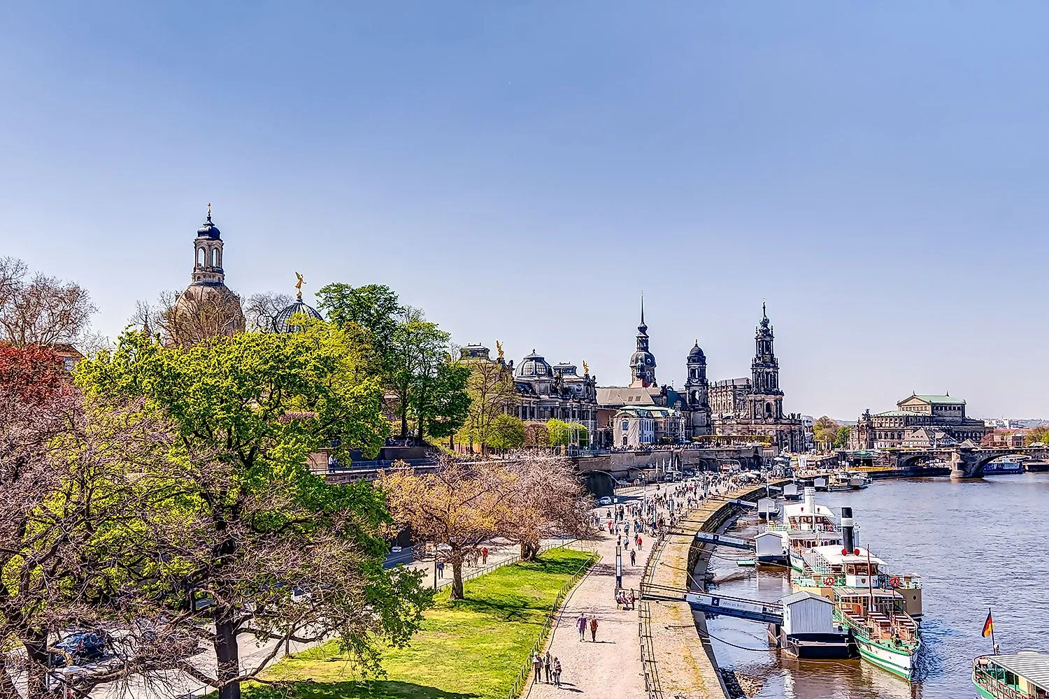 Belebte Promenade am Elbufer in Dresden mit Blick auf Frauenkirche, Hofkirche und Boote am Ufer bei Frühlingswetter