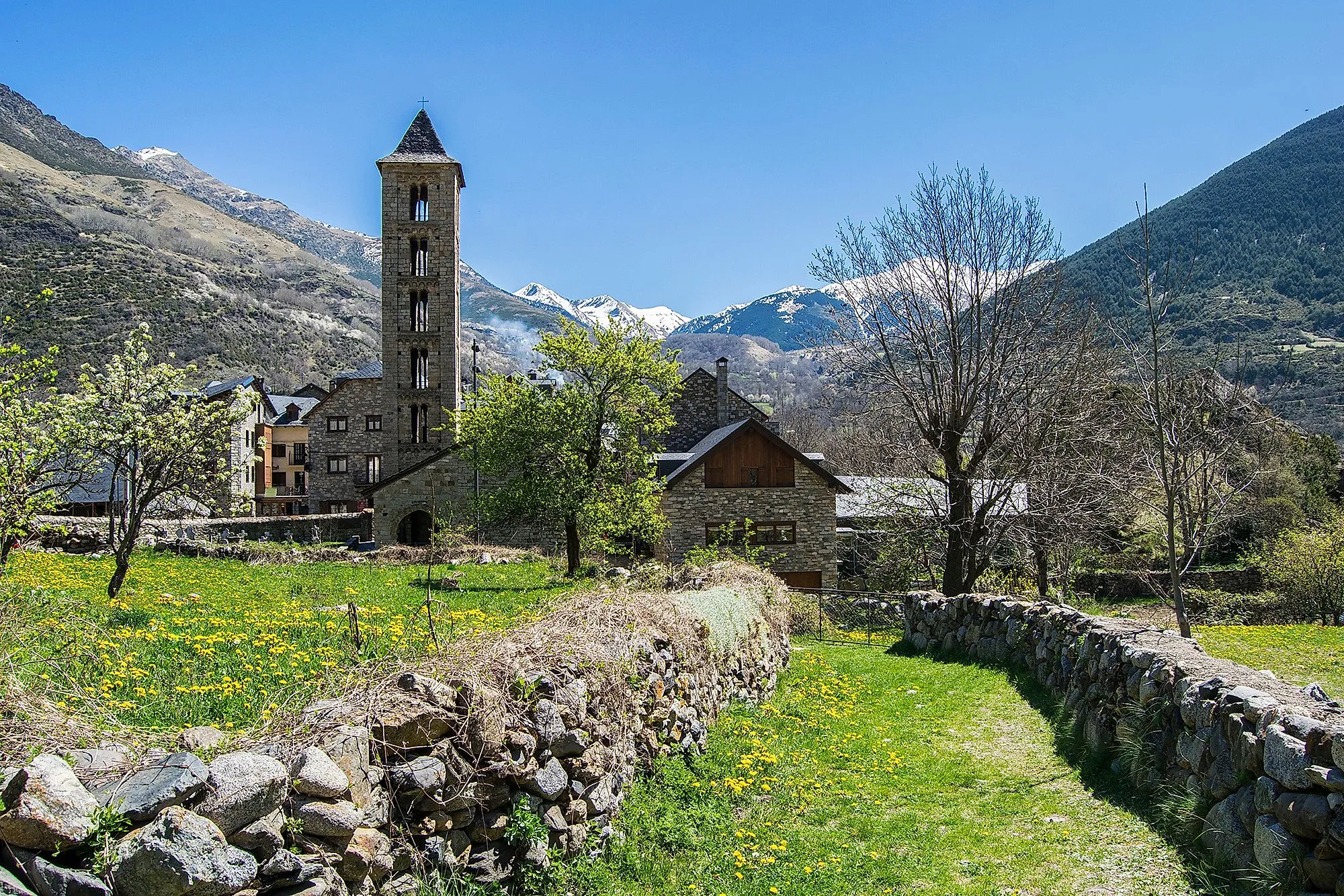 Steinkirche auf grüner Wiese im Vall de Boí mit Pyrenäen-Gipfeln im Hintergrund
