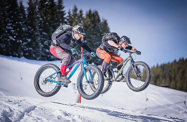 Dos ciclistas saltan con fatbikes en la nieve en el Postalm