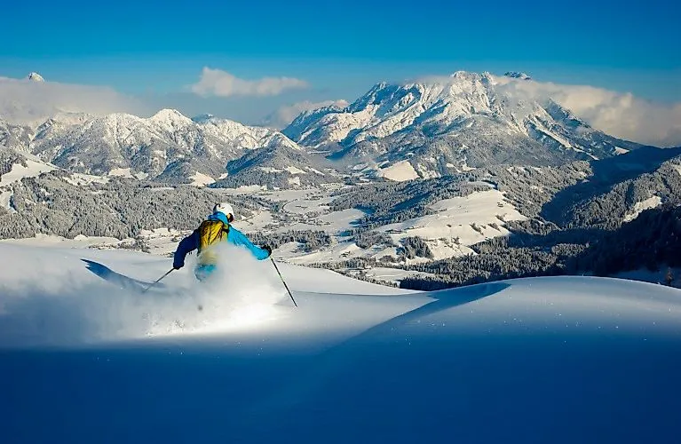 Freerider fährt durch tiefen Pulverschnee mit Blick auf die verschneite Berglandschaft von Fieberbrunn.