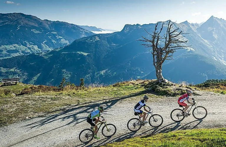Drei Mountainbiker fahren bei Sonnenschein über einen Panoramaweg in den Tiroler Alpen bei Fügen.