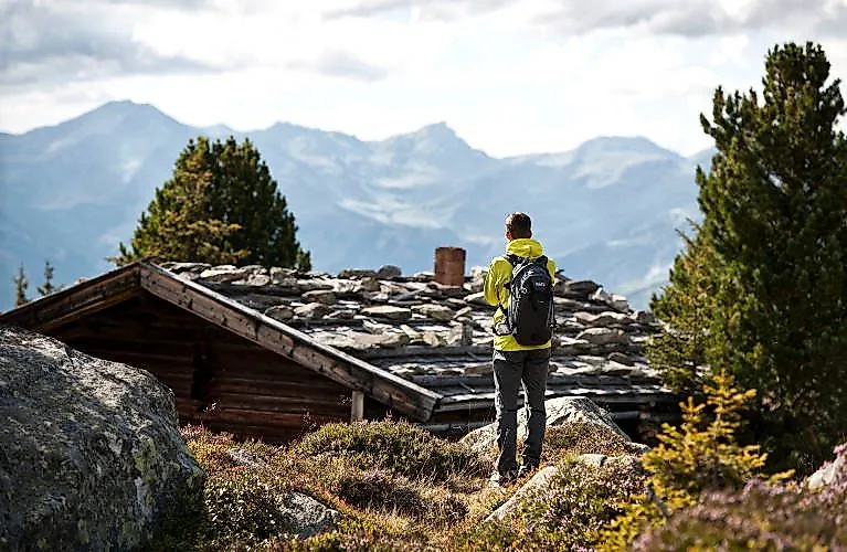 Wanderer mit Rucksack genießt die Aussicht auf die umliegenden Berge und eine Almhütte bei Fügen.