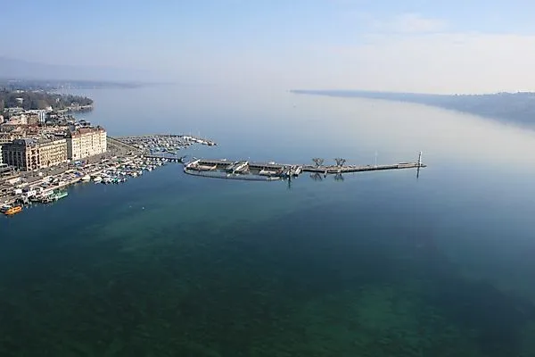 Weitläufiger Blick über den ruhigen Genfersee mit Hafenanlagen und klarer Sicht auf das Wasser