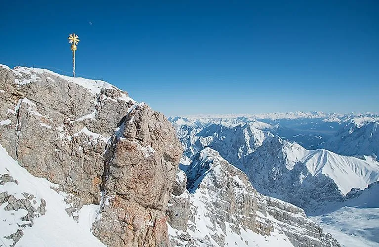 Snow-covered summit of the Zugspitze with summit cross and wide panoramic view in winter.