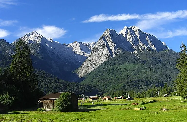 Blick auf sommerlich grüne Wiesen in Grainau, Bayern, im Hintergrund die schroffen Gipfel der Zugspitze