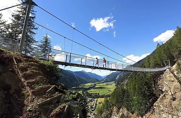 Zwei Wanderer überqueren eine schmale Hängebrücke mit Blick auf das Ötztal bei Längenfeld.