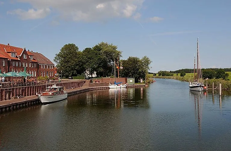 Boote im idyllischen Hafen von Hooksiel vor Backsteinhäusern und Bäumen an einem sonnigen Tag
