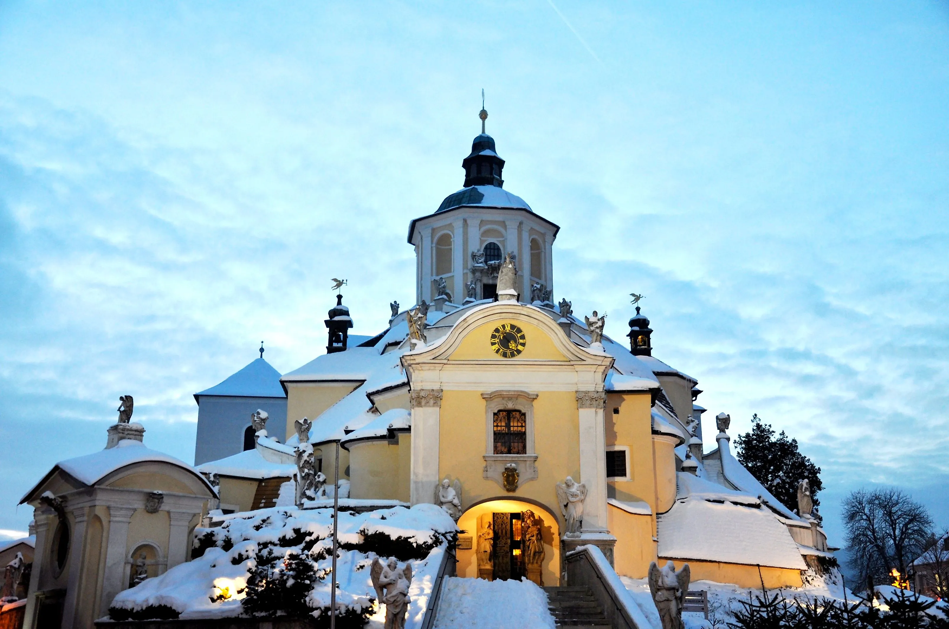 Die verschneite Haydnkirche in Eisenstadt, auch bekannt als Bergkirche, am frühen Abend mit beleuchteter Fassade.