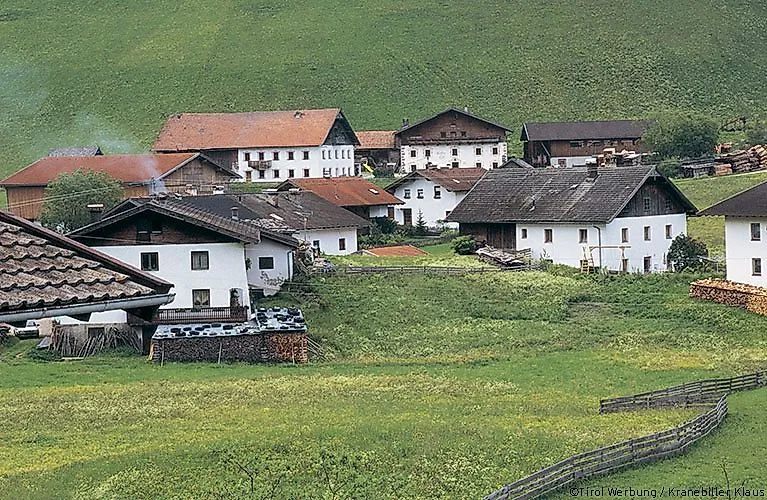 Traditionelles Tiroler Dorf mit historischen Bauernhäusern in Obernberg am Brenner, umgeben von grünen Wiesen am Fuße eines Hügels.