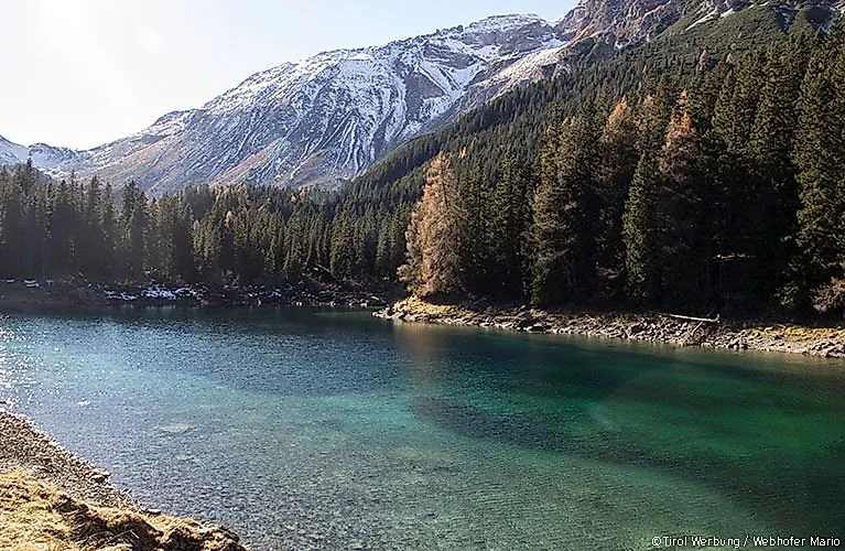 Der Obernberger See mit türkisblauem Wasser, eingerahmt von dichten Wäldern und verschneiten Bergen im Wipptal.