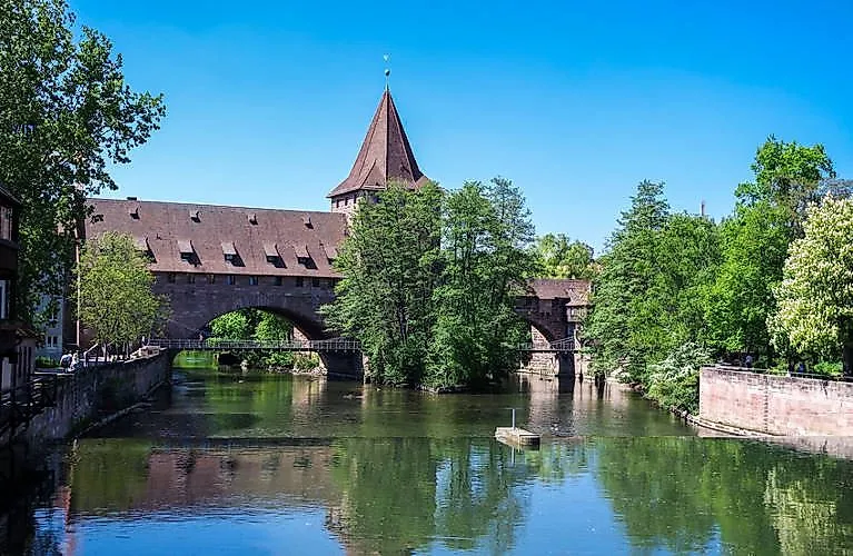 Alte Brücke mit Turm über die Pegnitz, umgeben von Bäumen in der Altstadt von Nürnberg.