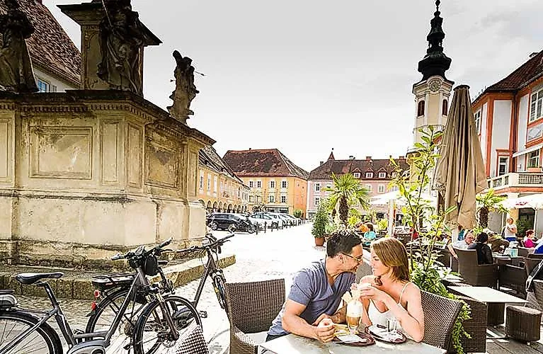 Pár si vychutnáva kávu na historickom hlavnom námestí Bad Radkersburgu v Štajersku za letného počasia.