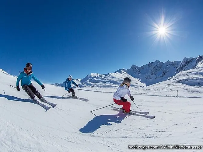 Drei Skifahrer auf perfekt präparierter Piste am Hochzeiger im Pitztal unter strahlender Wintersonne.