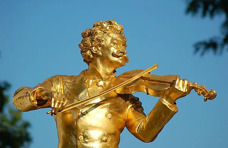 Goldene Statue von Johann Strauss mit Geige vor blauem Himmel im Salzburger Stadtpark
