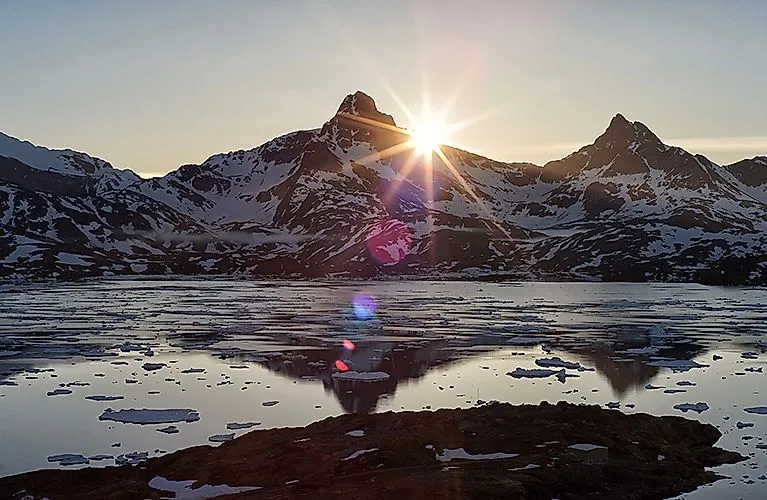 Sonnenuntergang über schneebedeckten Bergen und Eisschollen an der Bucht in Tasiilaq