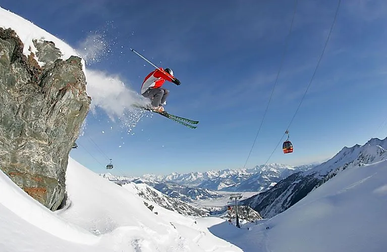 Skifahrer springt über eine Felskante am Kitzsteinhorn in Kaprun mit Blick auf das verschneite Alpenpanorama.