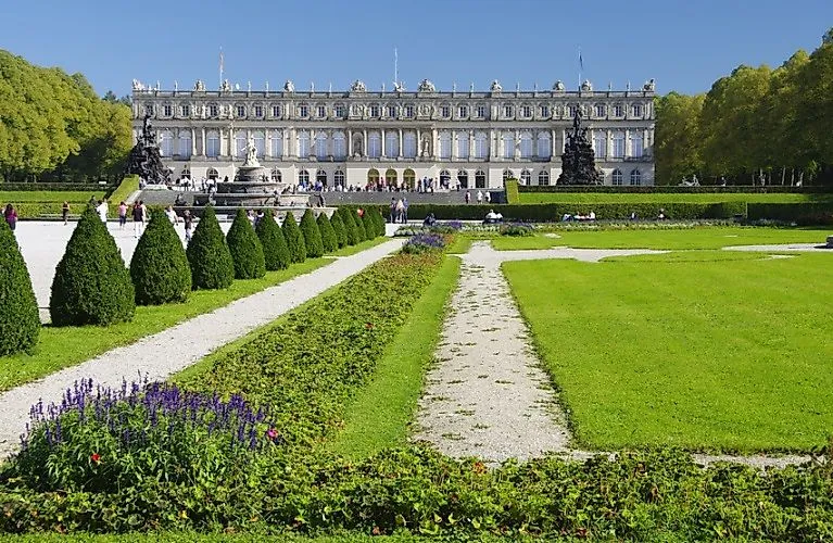 Barocke Schlossfassade von Herrenchiemsee mit Besuchern und gepflegtem Schlossgarten bei Sonnenschein am Chiemsee