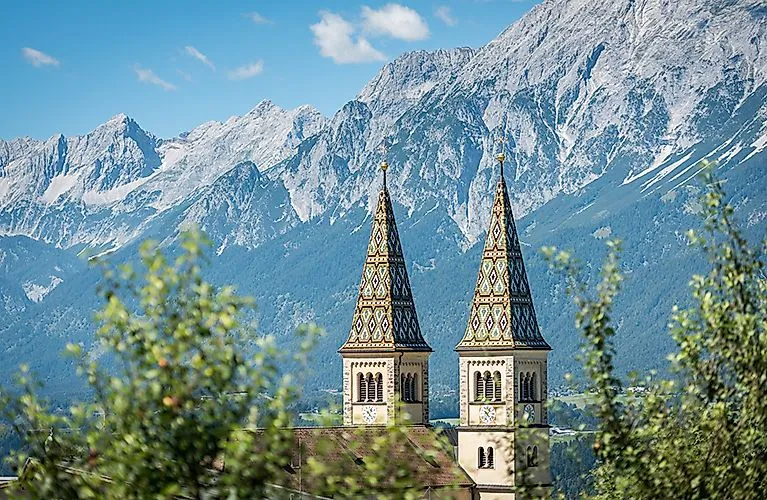 Zwei verzierte Kirchtürme ragen vor dem Karwendelgebirge bei klarem Sommerwetter in den Himmel.