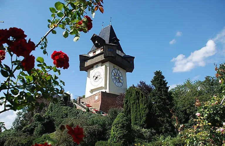 Der historische Uhrturm auf dem Schlossberg in Graz, umgeben von blühenden Rosen und grüner Vegetation an einem sonnigen Sommertag.