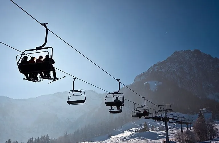 Skifahrer im Sessellift mit Blick auf verschneite Berge im Skigebiet Kössen bei Sonnenschein und klarem Winterhimmel