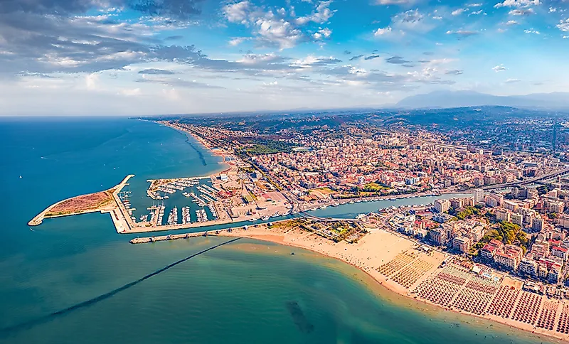 Küstenstadt mit Hafen, Strand und dicht bebautem Ort an einem langen Sandstrand unter blauem Himmel