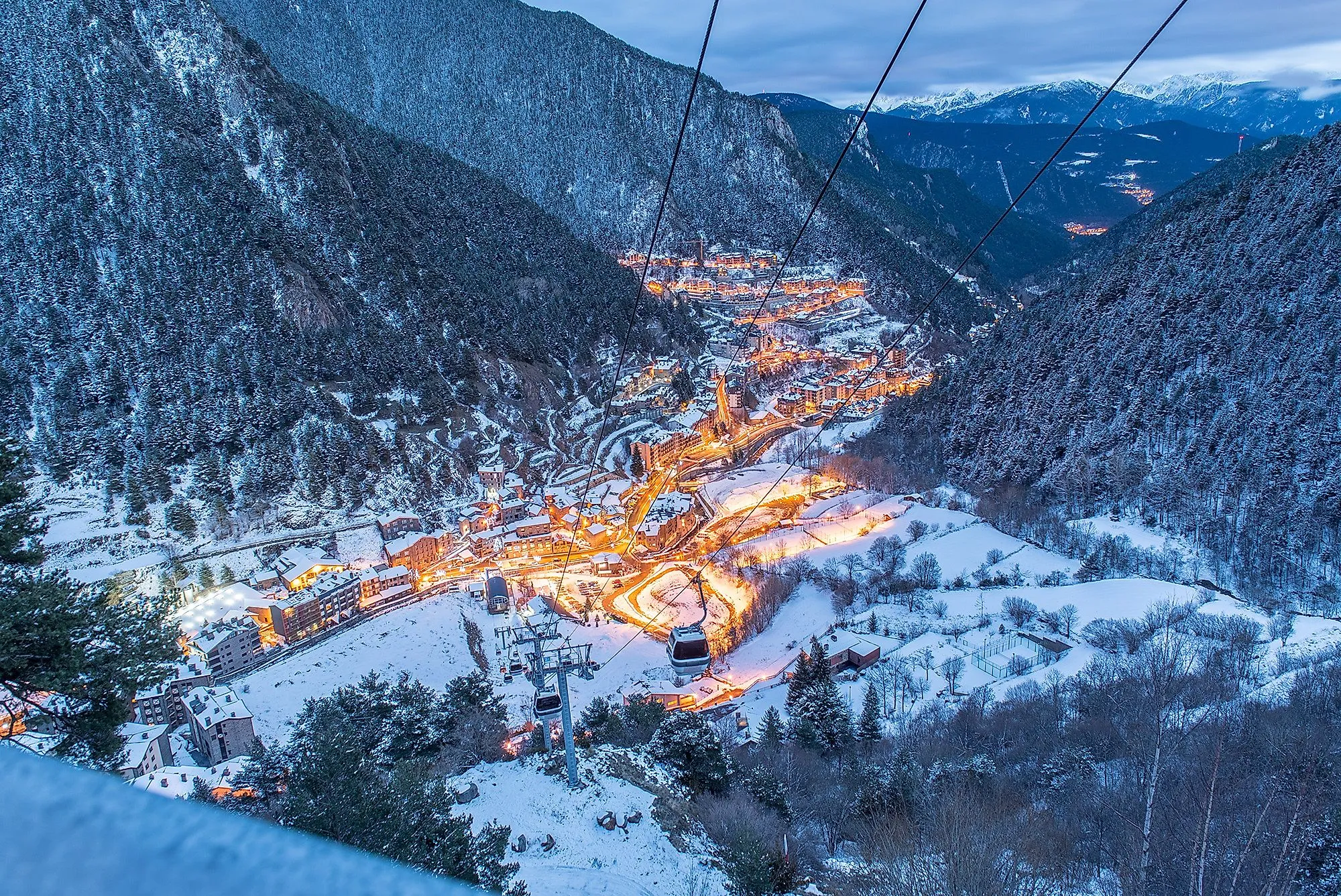 Verschneites Arinsal in Andorra mit beleuchteten Straßen und Seilbahn am Winterabend