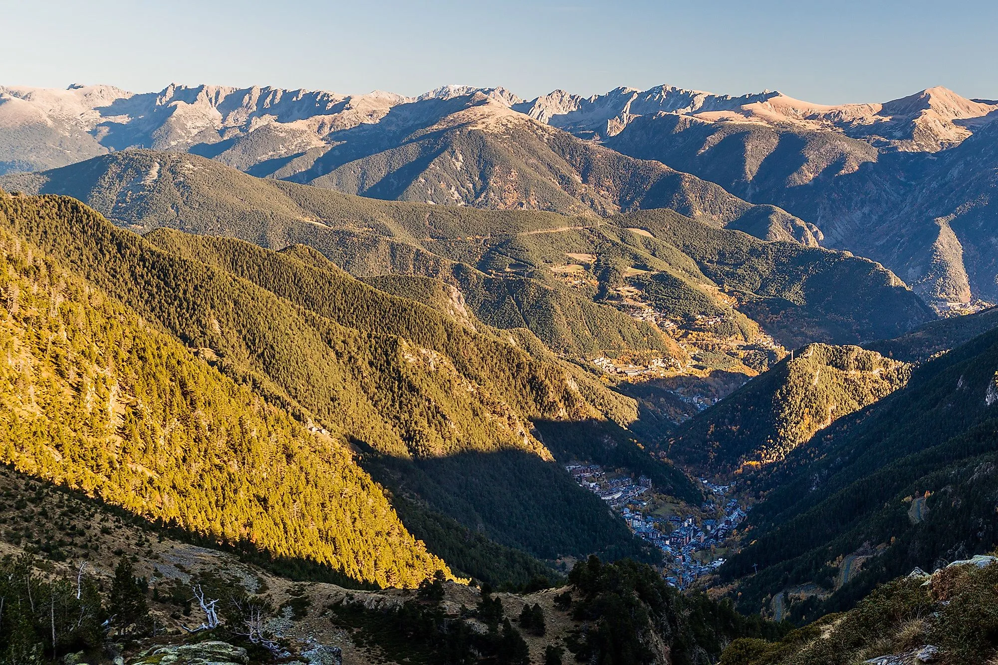 Vogelperspektive auf grüne Berghänge und das Dorf Arinsal in Andorra an einem klaren Sommertag