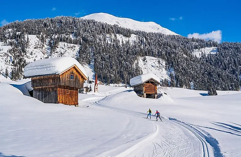 Dvaja bežkári na slnečnej trase medzi zasneženými chatami v údolí Lesachtal