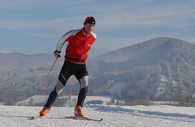 Langläufer in roter Kleidung auf verschneiter Loipe bei Bad Tölz vor bewaldeter Winterkulisse.