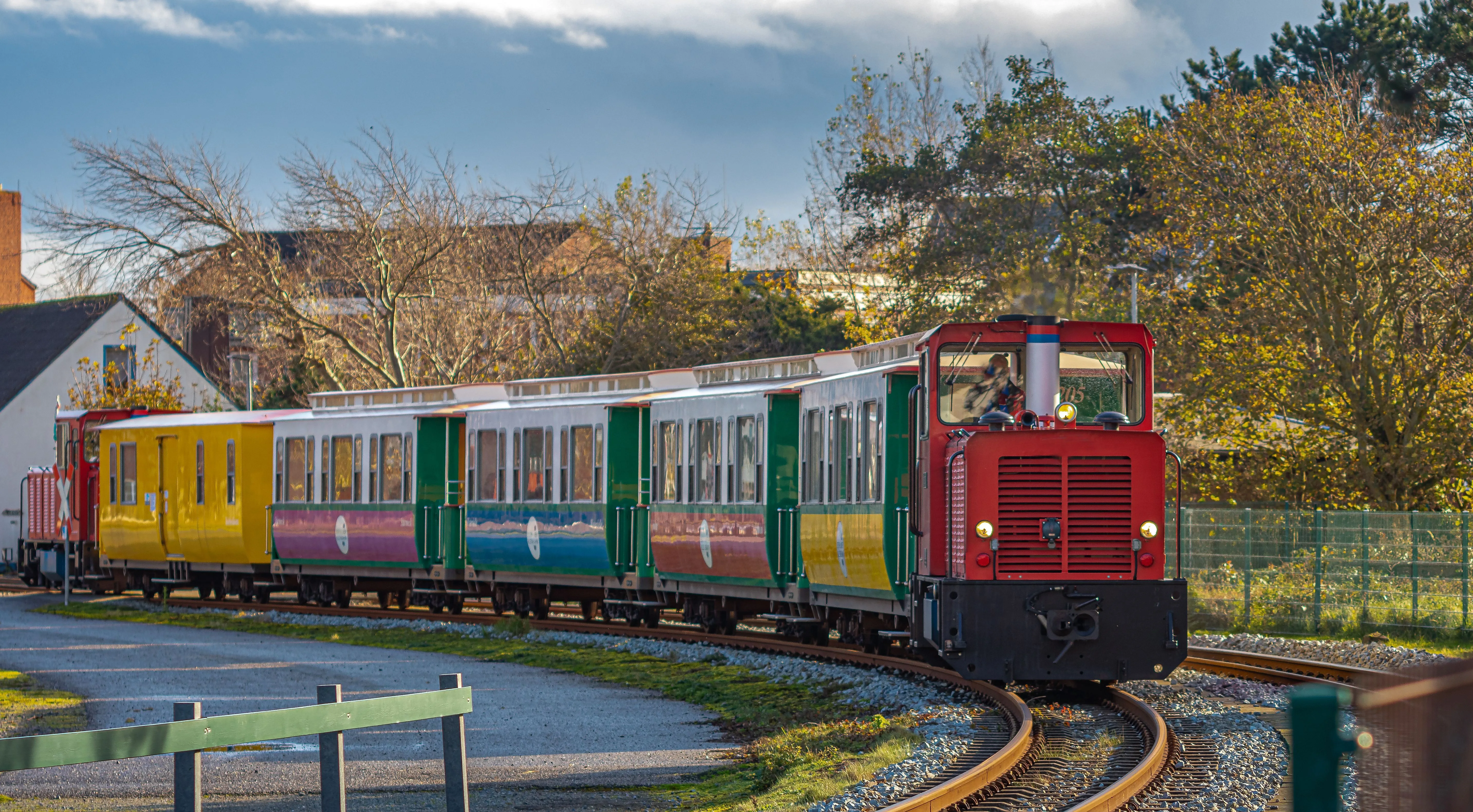 Bunte Inselbahn auf Borkum fährt durch herbstliche Landschaft mit historischen Waggons.
