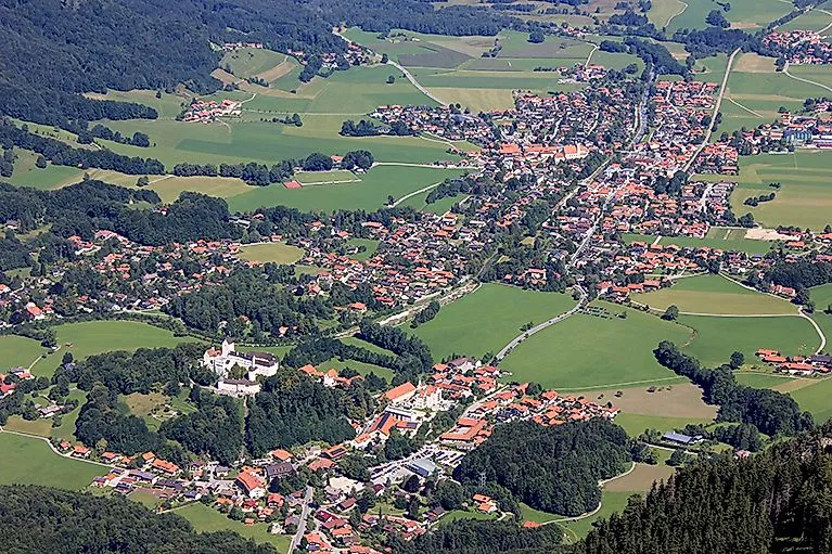 View of Aschau im Chiemgau with Hohenaschau Castle, surrounded by green meadows and forests.
