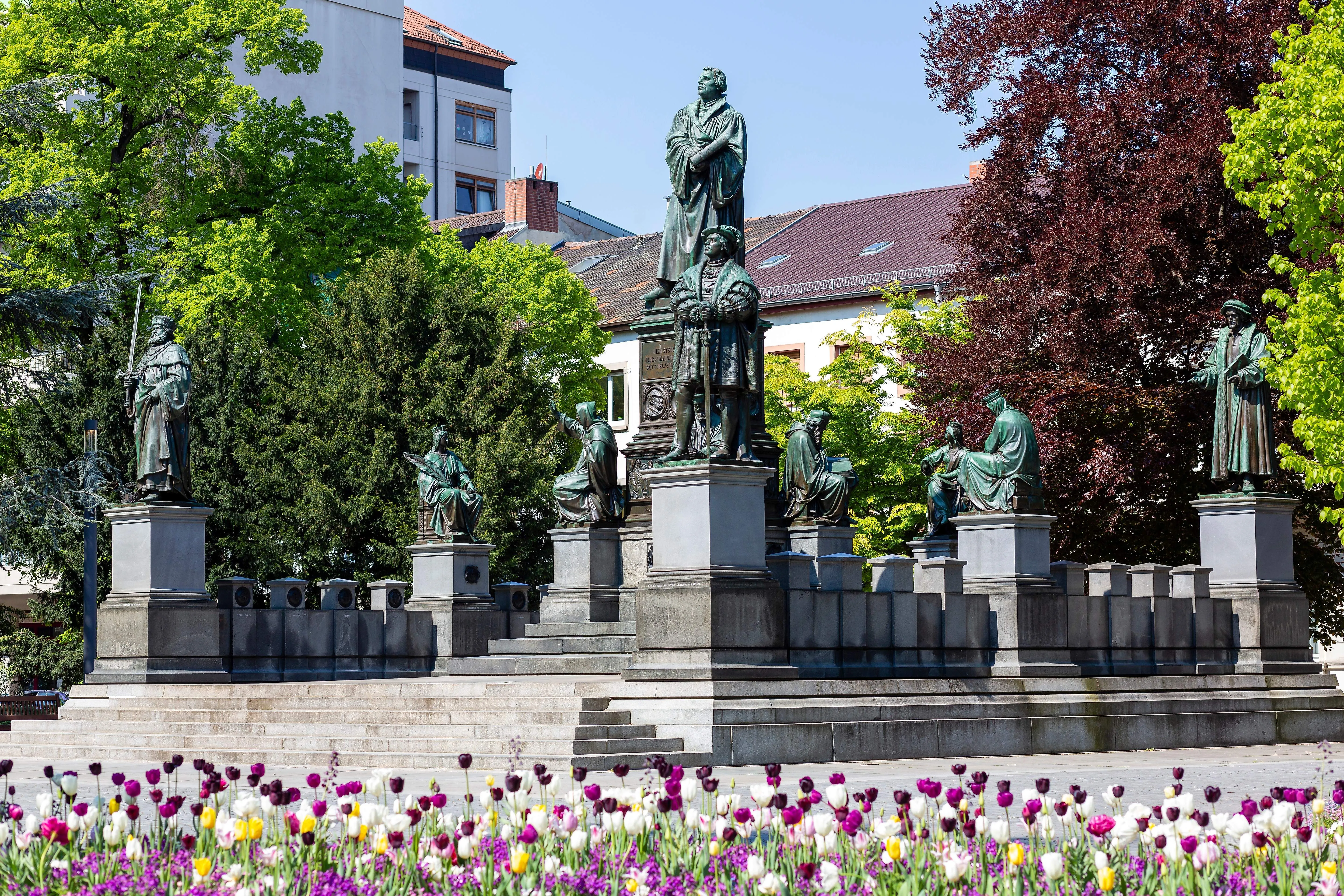 Das Martin-Luther-Denkmal in Worms mit umliegenden Skulpturen und blühenden Tulpen.
