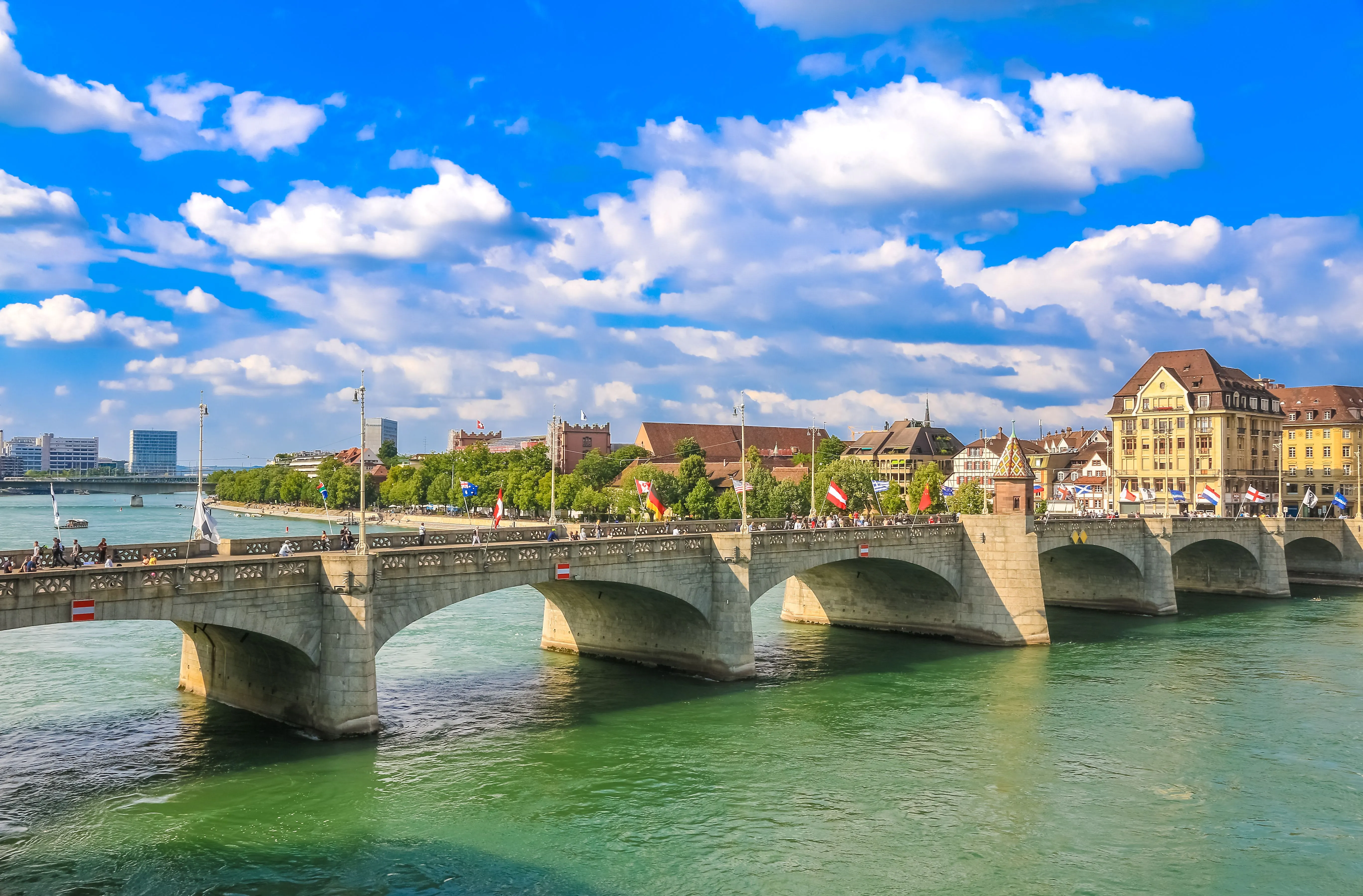 Blick auf die Mittlere Rheinbrücke mit wehenden Flaggen und die Altstadt in Basel an einem strahlenden Sommertag