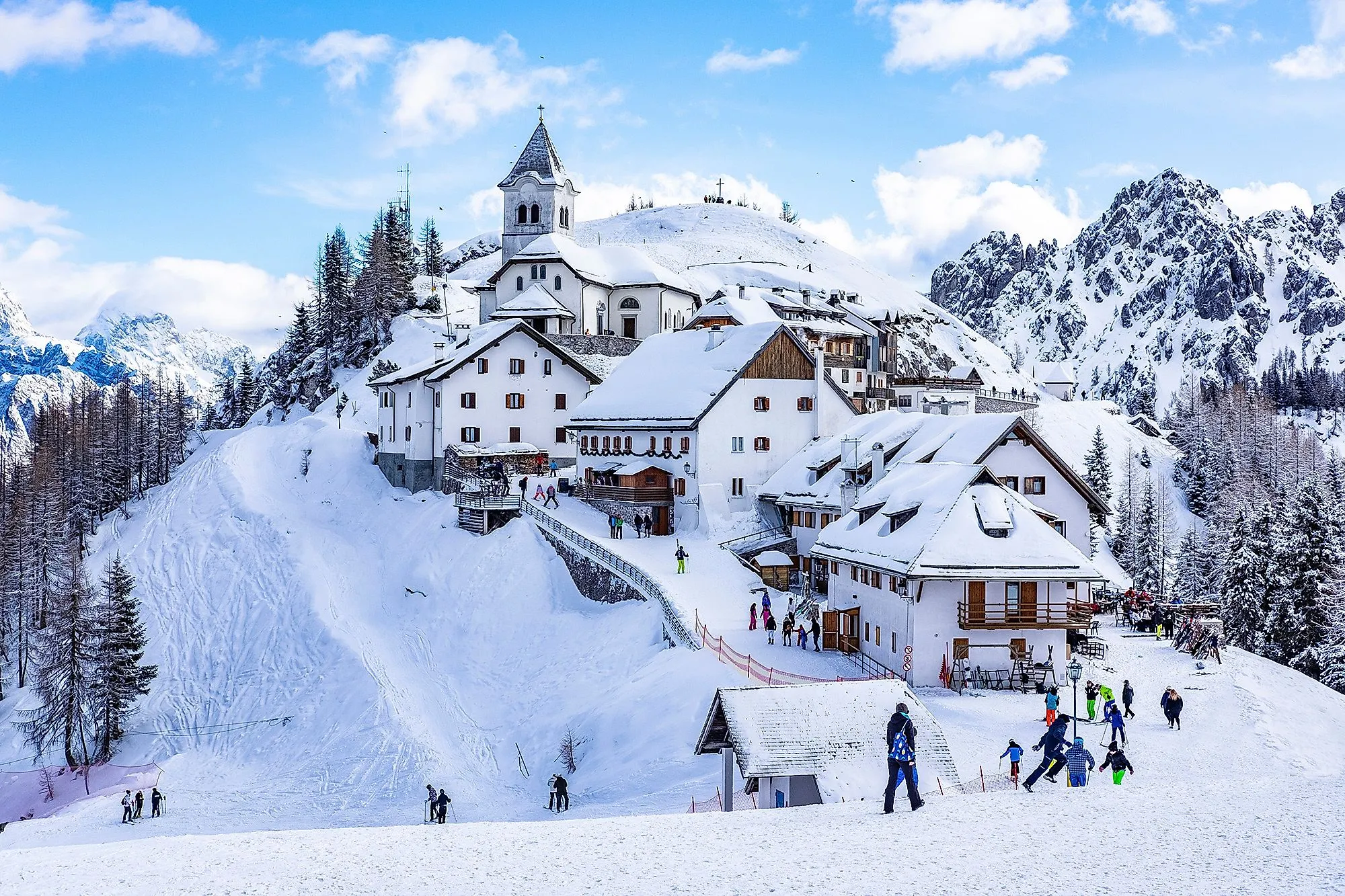 Winterliches Monte Lussari mit verschneiten Häusern und Skifahrern in Tarvisio