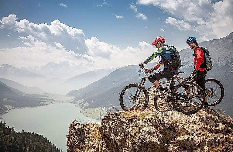 Zwei Mountainbiker genießen die Aussicht über den Reschensee in Nauders.